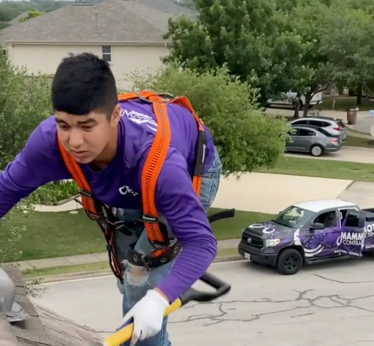 A Mammoth roofer tears off old shingles with a shovel, a wrapped Mammoth truck parked in the street below